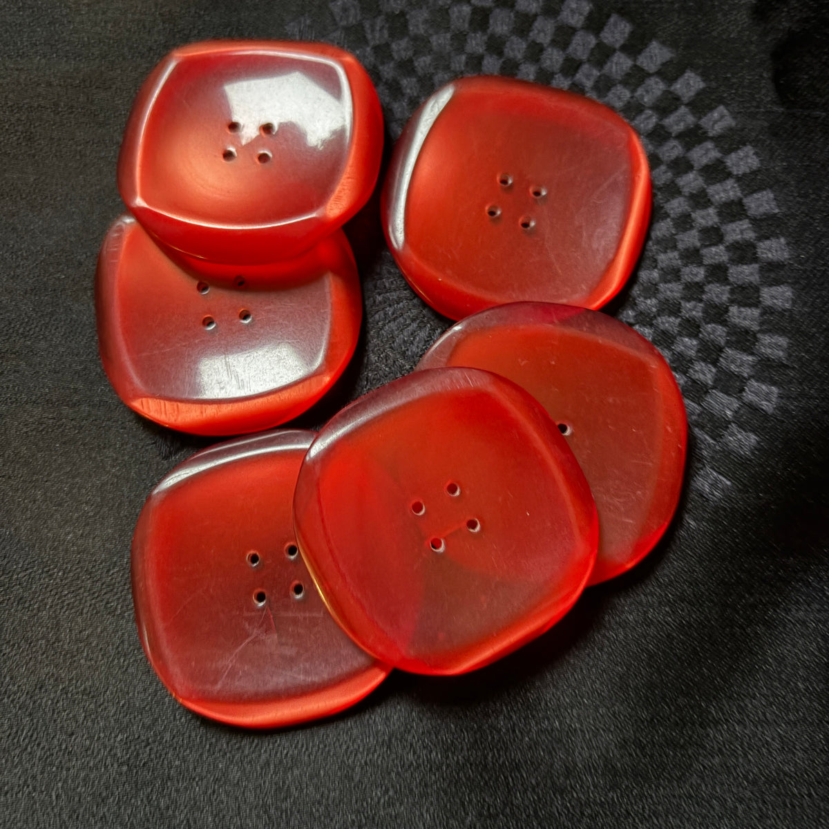 Stack of square red glass coat buttons on black fabric