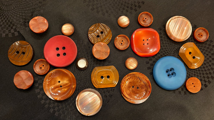a variety of large and medium buttons in browns and reds, with one blue. All set on a black fabric.