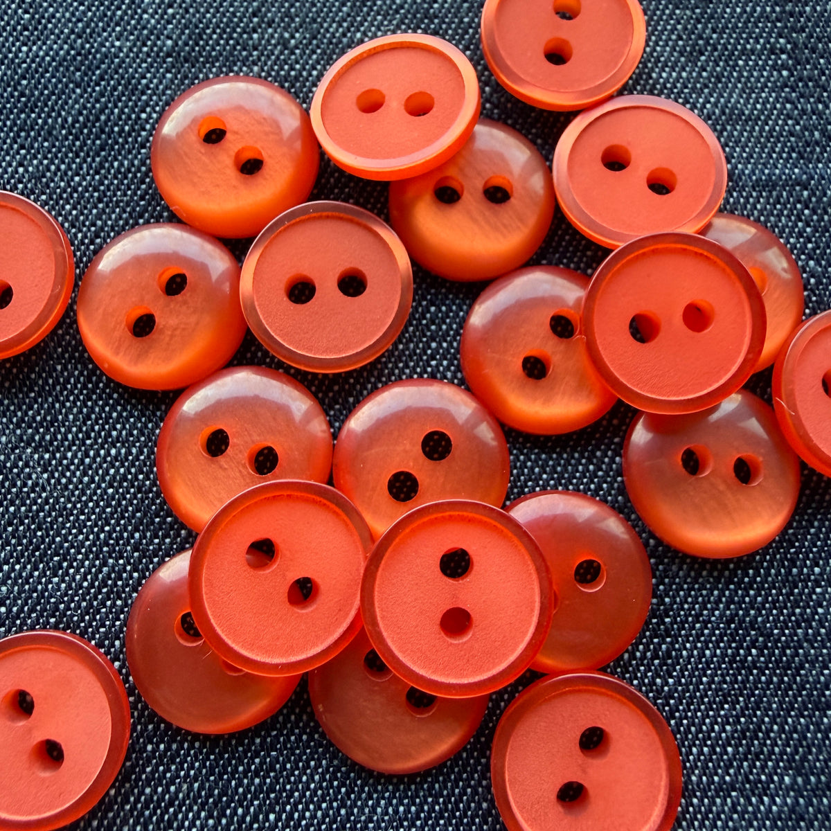 Pile of orange two-hole plastic shirt buttons on denim