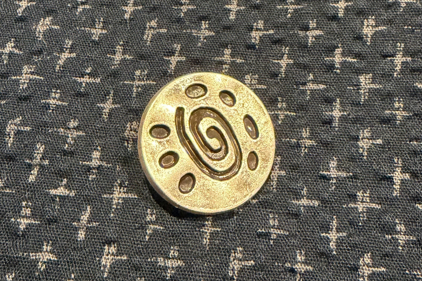 Silver button on a dark fabric with white cross patterns