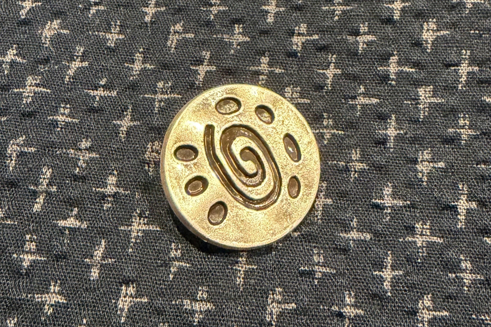 Silver button on a dark fabric with white cross patterns