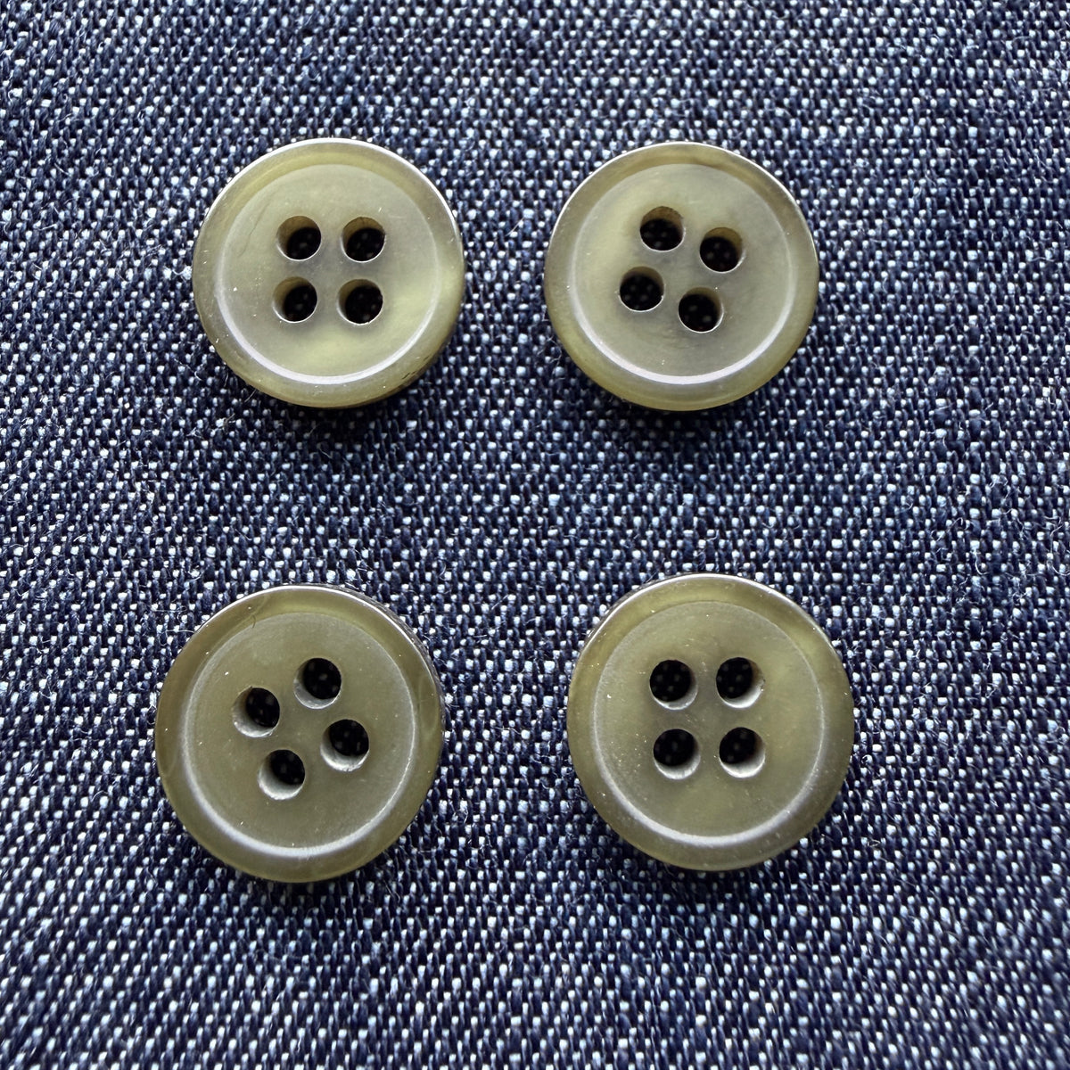 Glossy olive four-hole plastic shirt buttons on denim