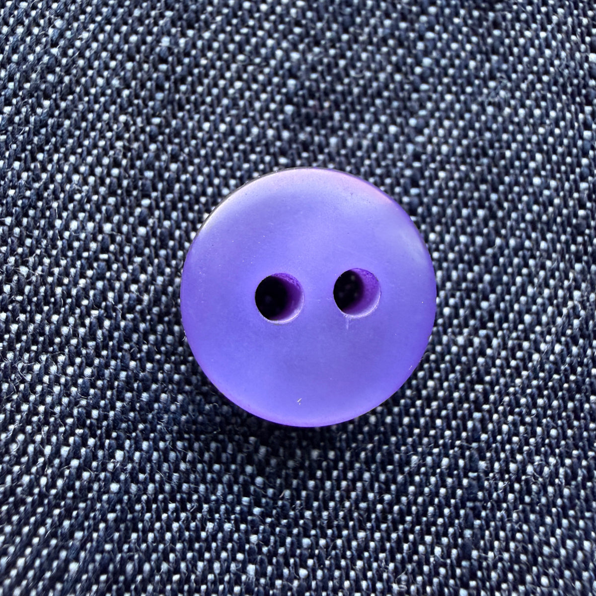 Close-up of thick purple plastic shirt buttons with a pearly swirl