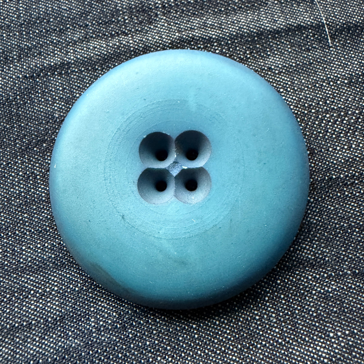 Matte blue 48 mm casein button with four holes set in a sunken cloverleaf.