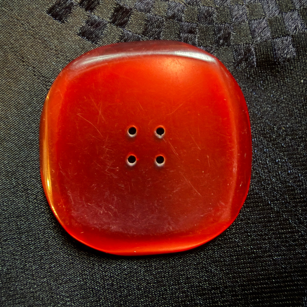 Close-up of a square red glass button with a dished centre and four holes