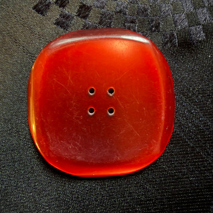 Close-up of a square red glass button with a dished centre and four holes