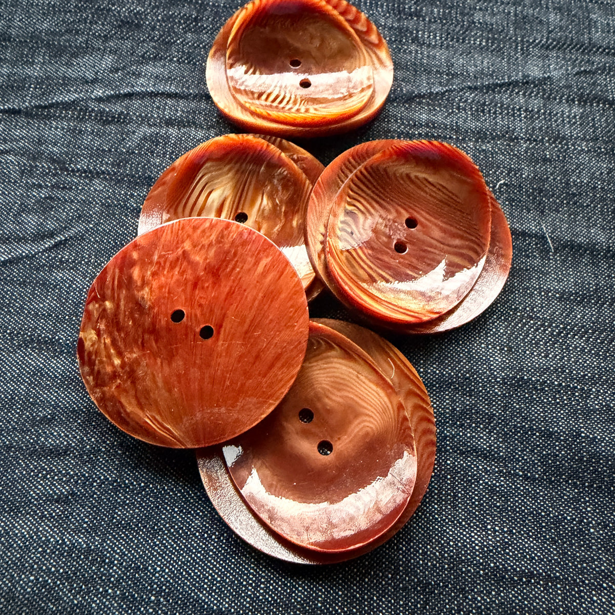 Rust swirl statement buttons stacked, showing the flat back and curled front.