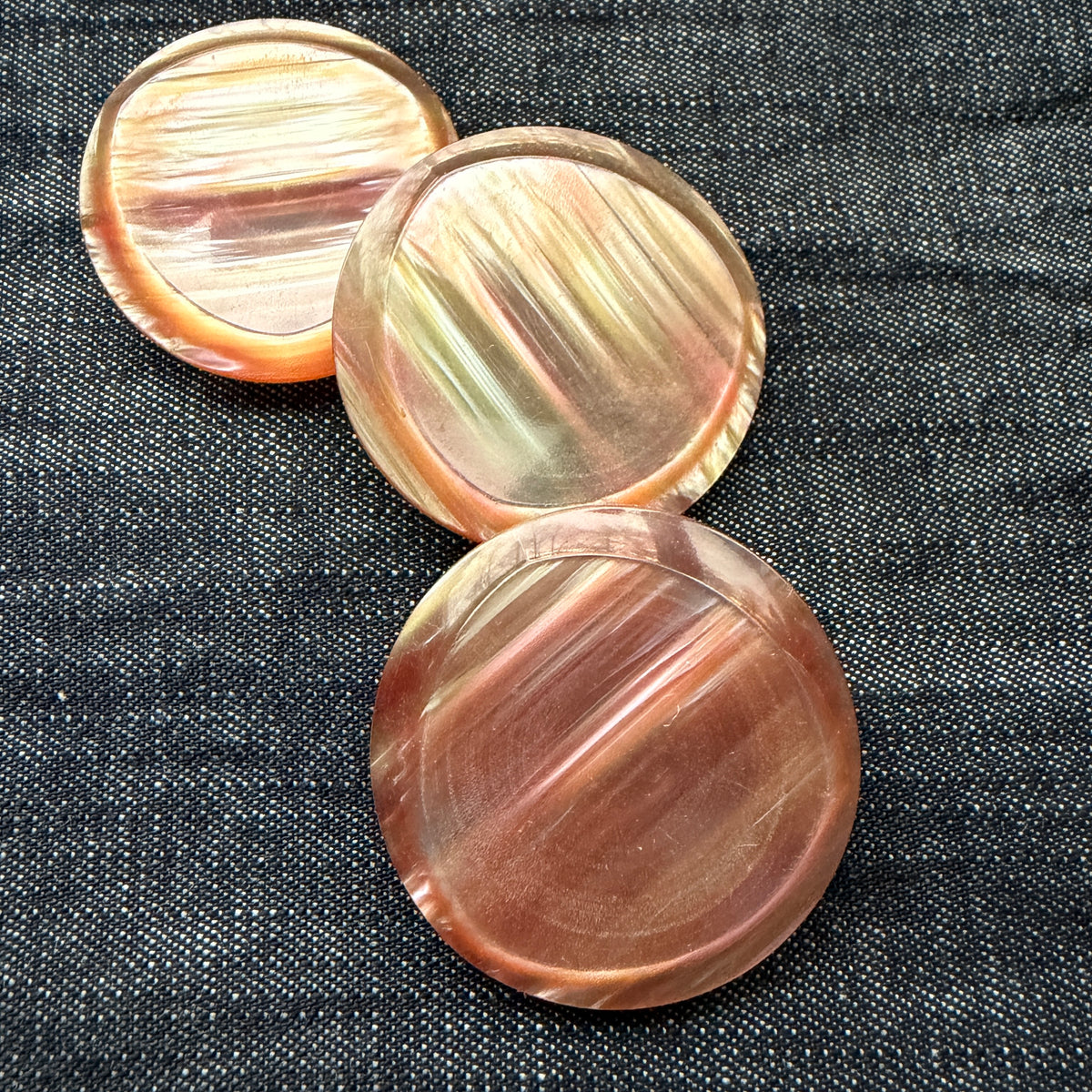 Three rose-gold casein statement buttons on denim, each with a slightly different pattern.