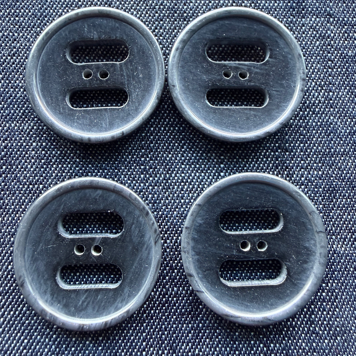 Four grey plastic coat buttons with two wide slots and two small holes