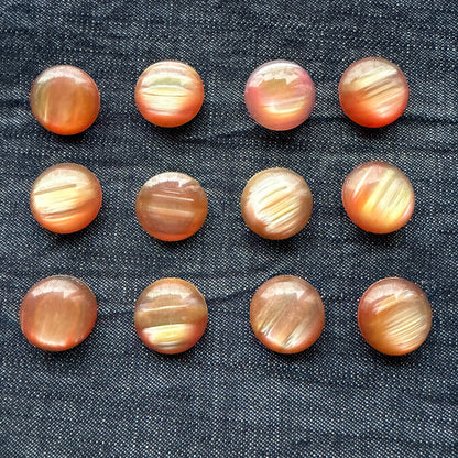 Twelve rose-gold domed casein buttons arranged in rows on denim.