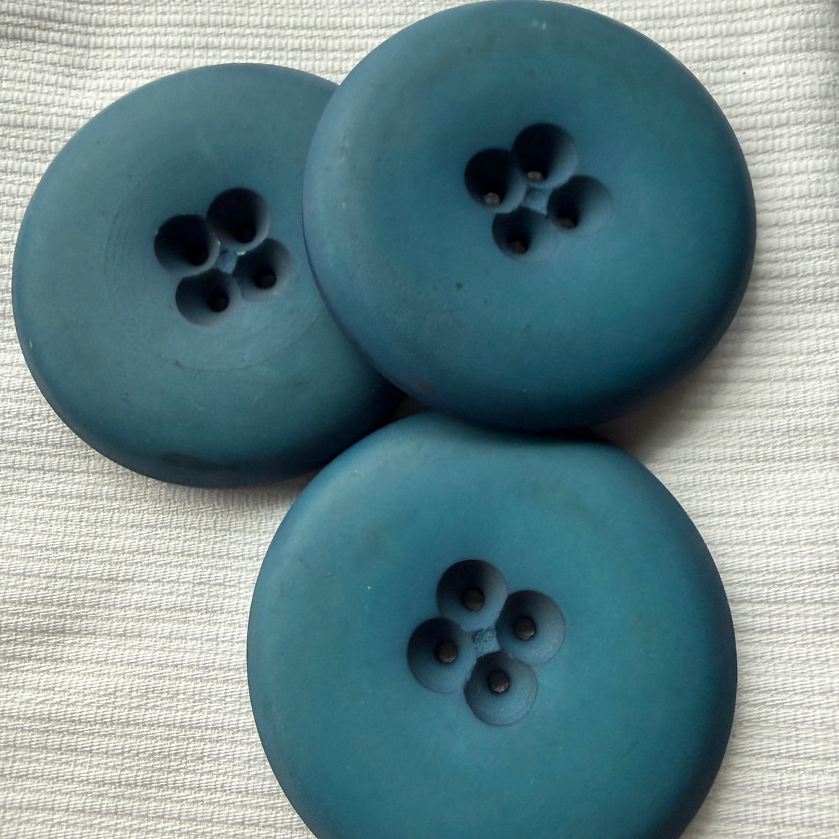 Blue casein buttons on white fabric, where the colour reads a shade deeper.
