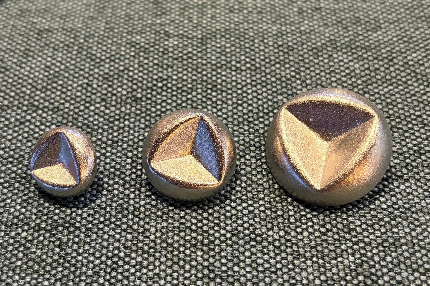 Set of metallic buttons on a textured surface with packaging in the background.