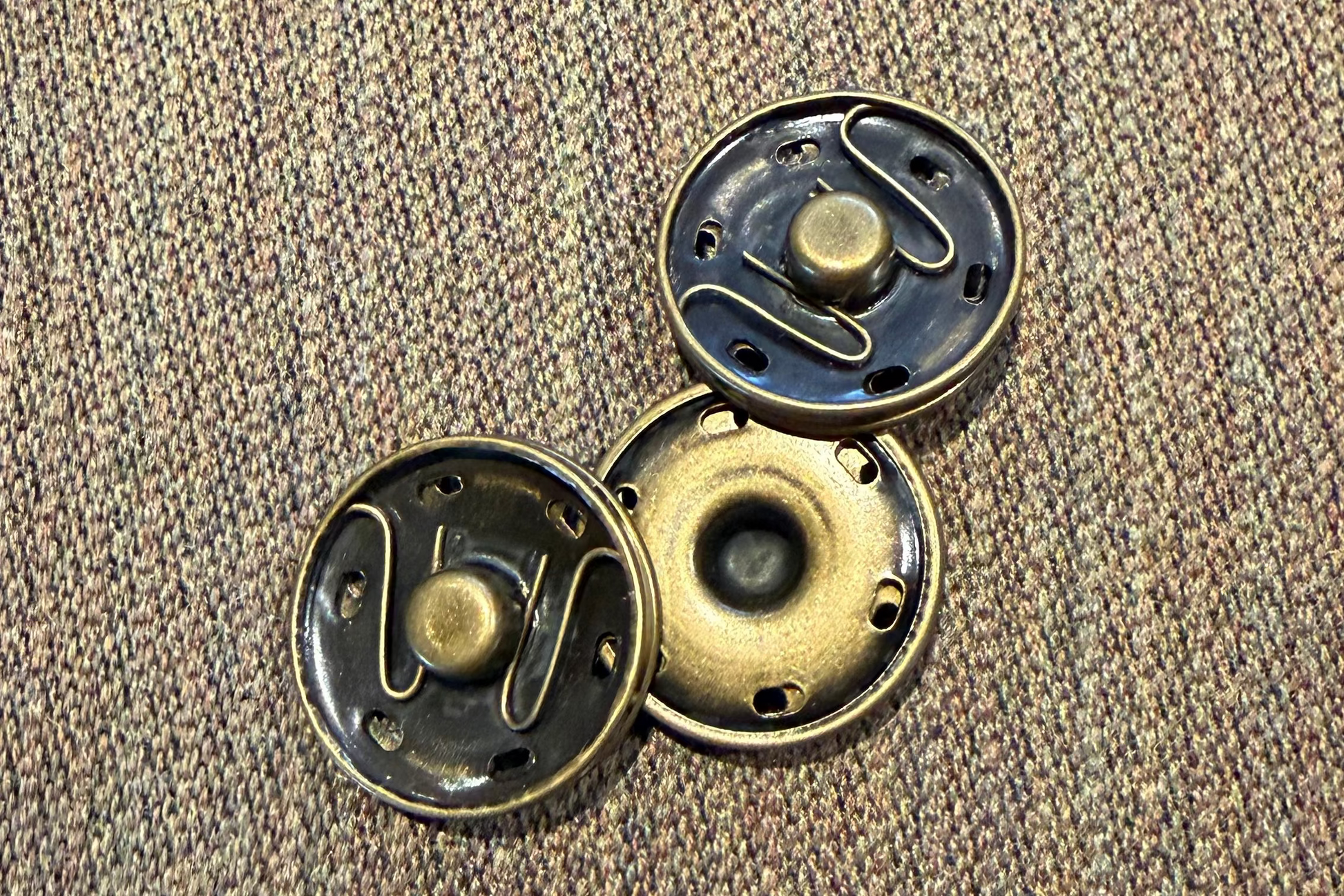 Three metallic snaps on a textured brown fabric background