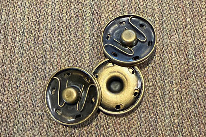 Three metallic snaps on a textured brown fabric background